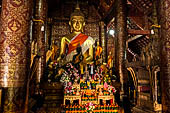 Wat Xieng Thong temple in Luang Prabang, Laos.  The main Buddha of the sim sits on a platform, surrounded by smaller statues, candles, and offerings. 